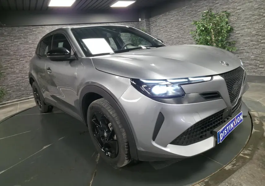 Vue 3/4 avant droite de l'Alfa Romeo Junior 1.2 hybride gris métallisé avec jantes noires et phares LED allumés.