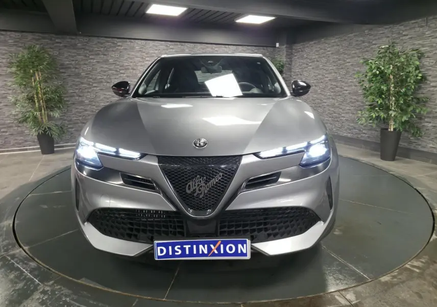 Vue avant d'une Alfa Romeo Junior 1.2 Ibrida gris métallisé avec calandre noire et feux LED allumés.