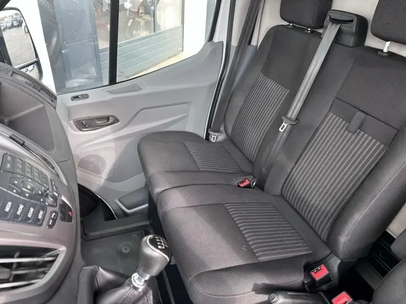 Vue intérieure côté conducteur du Ford Transit Fourgon blanc 2019, montrant les sièges avant noirs et le levier de vitesse manuel.