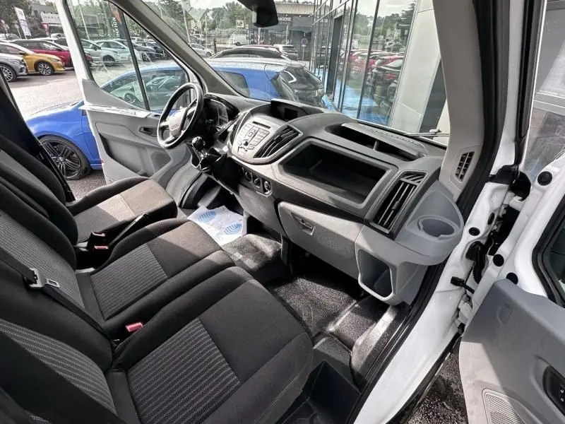 Intérieur du Ford Transit Fourgon blanc 2019, vue côté conducteur ouverte, montrant tableau de bord et sièges noirs.