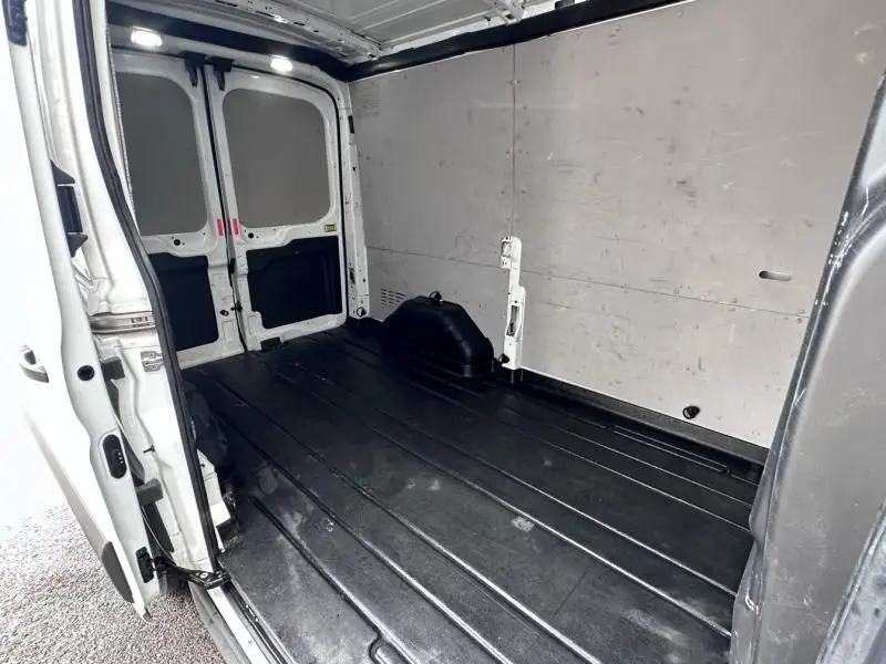 Intérieur vide du fourgon Ford Transit blanc, vue depuis l'arrière avec portes ouvertes, sol noir et parois claires.