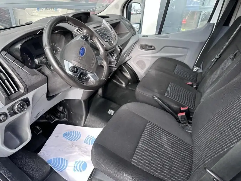 Vue intérieure côté conducteur du Ford Transit Fourgon blanc 2019, montrant le volant, tableau de bord et sièges noirs.