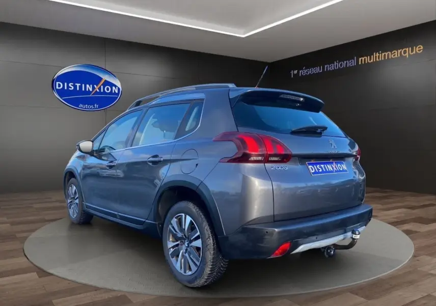 Peugeot 2008 gris foncé vue 3/4 arrière droit, avec spoiler de toit et jantes alliage visibles.
