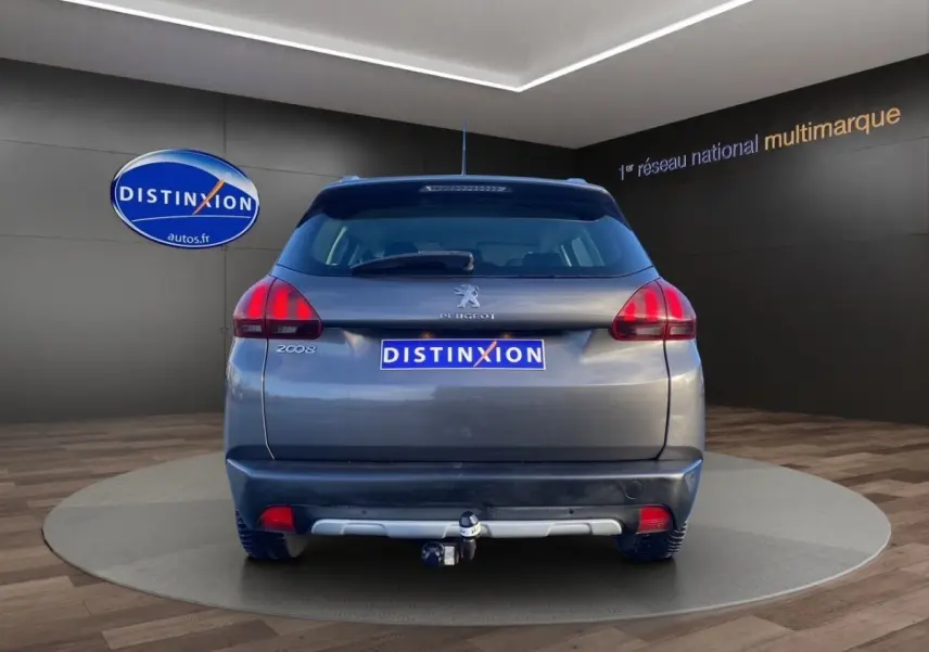 Vue arrière d’un Peugeot 2008 gris foncé avec spoiler de toit et attelage de remorque visible en intérieur showroom.