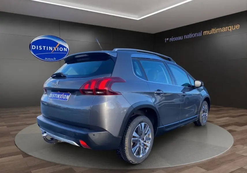 Peugeot 2008 gris foncé vue 3/4 arrière droit, avec spoiler de toit et jantes alliage visibles.