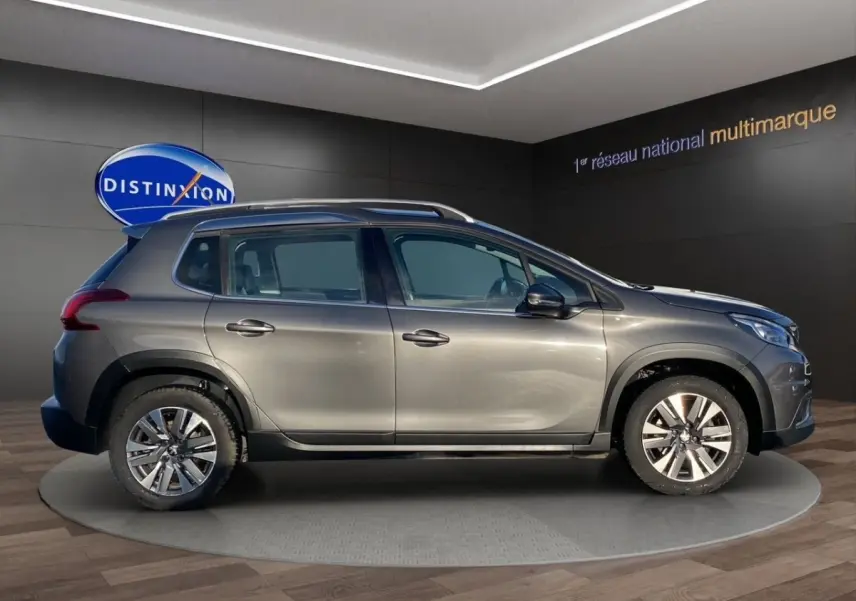 Vue latérale droite d’un Peugeot 2008 gris foncé avec rails de toit chromés dans un showroom.