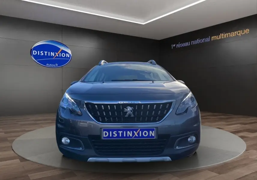 Vue frontale d'un Peugeot 2008 gris foncé avec calandre distinctive et feux LED dans un showroom.