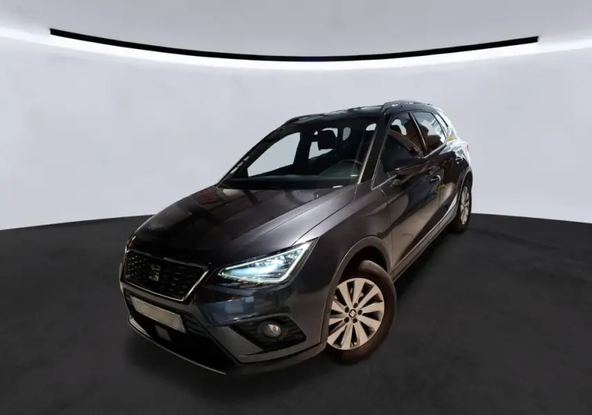 SEAT Arona gris foncé vue 3/4 avant droit, phares allumés et jantes alliage, dans un studio lumineux.