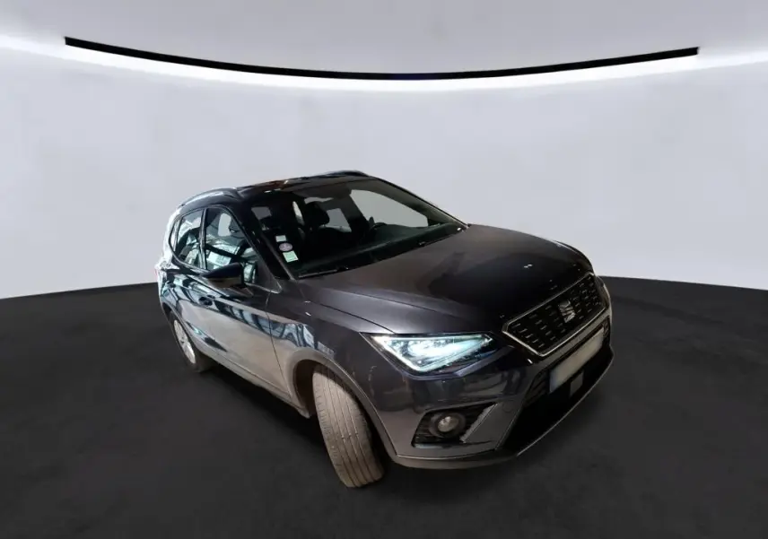 SEAT Arona gris foncé en 3/4 avant droit, phares allumés, sur fond neutre en studio.