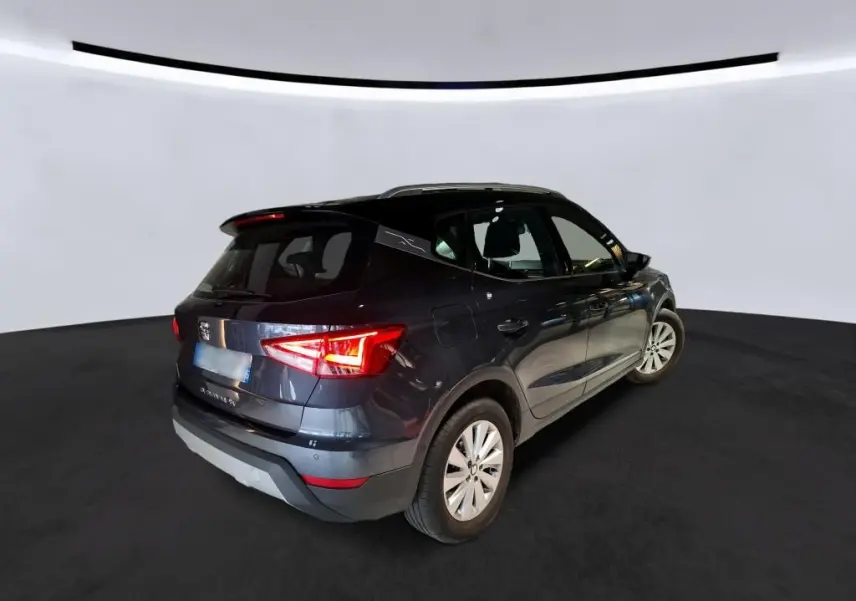 SEAT Arona gris foncé vue 3/4 arrière droit, avec feux arrière allumés et jantes argentées, sur fond neutre.