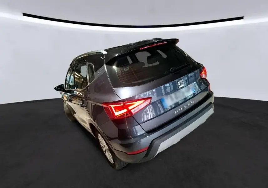 Vue 3/4 arrière droite d'un SEAT Arona gris foncé avec feux arrière allumés dans un studio lumineux.