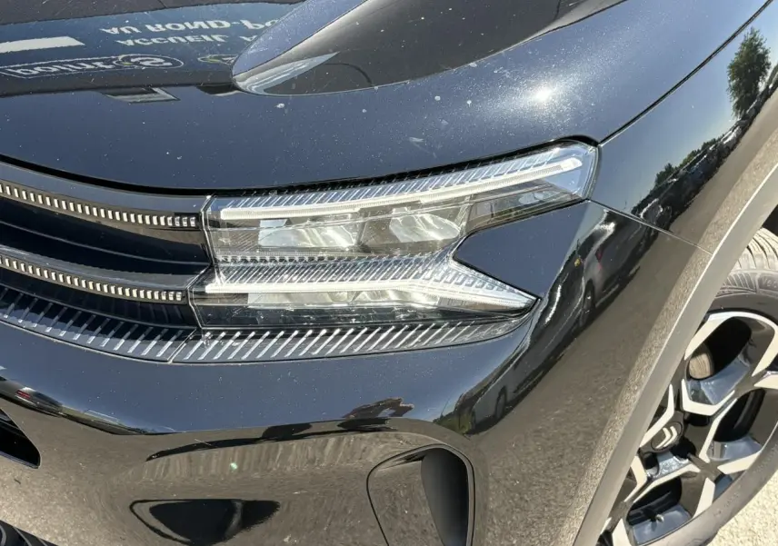 Gros plan sur le phare avant droit du Citroën C5 Aircross Hybrid noir Perla avec jante alliage visible.