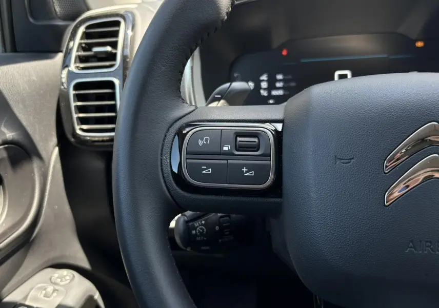 Gros plan sur le volant noir du Citroën C5 Aircross Hybrid 2025, avec commandes intégrées et aérateurs chromés en arrière-plan.