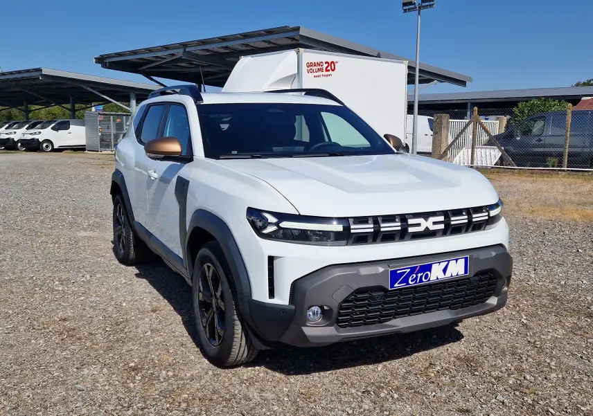 Vue 3/4 avant gauche d'un Dacia Duster blanc 2026 avec rétroviseurs bronze et calandre distinctive noire.