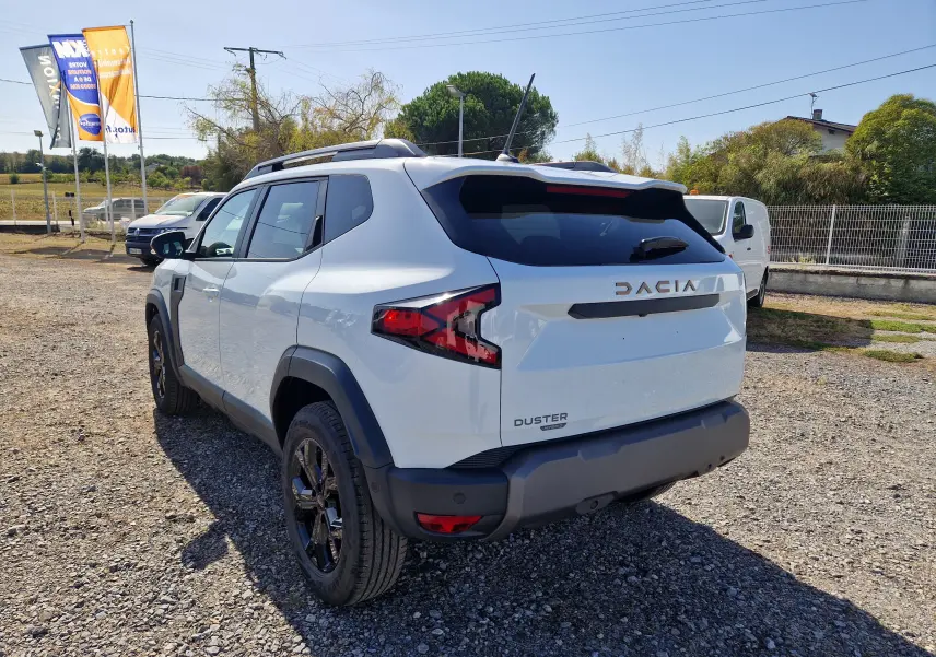 Vue 3/4 arrière droite d’un Dacia Duster blanc 2026 avec jantes noires et logo Dacia bien visible sur le hayon.