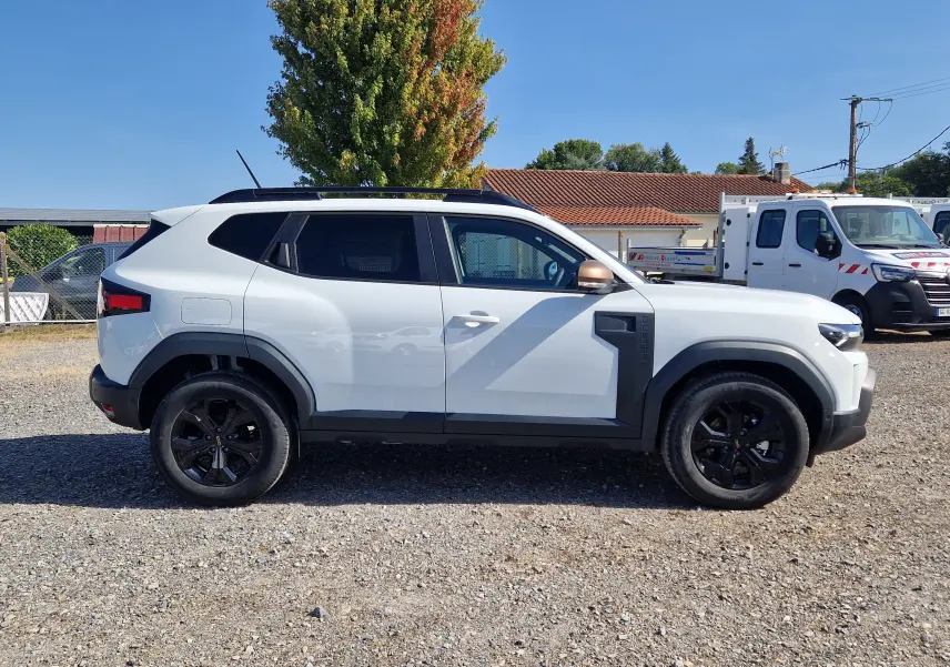 Profil droit du Dacia Duster blanc 2026 avec jantes noires et détails noirs contrastants sur les ailes et portes.