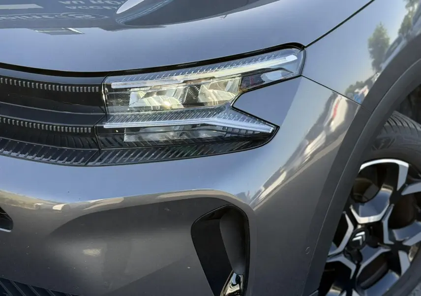 Gros plan sur l'avant droit gris Platinium du Citroën C5 Aircross Hybrid 2025 avec phare LED et jante alliage bi-ton.