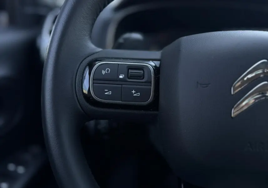 Gros plan sur les commandes gauche du volant noir du Citroën C5 Aircross Hybrid gris Platinium, intérieur moderne.