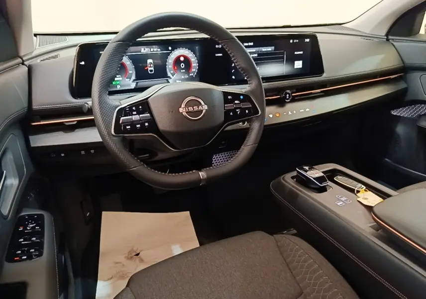 Vue intérieure avant du Nissan Ariya noir 2026, volant cuir multifonctions et grand écran tactile panoramique.
