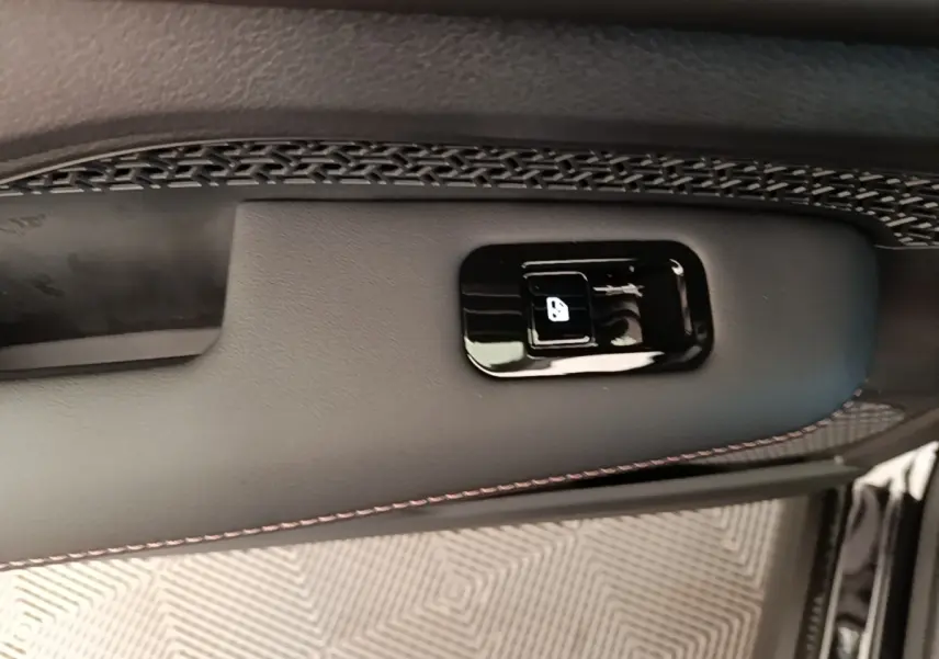 Gros plan sur la commande de verrouillage de porte noire intégrée à la garniture intérieure noire avec surpiqûres rouges du Nissan Ariya.