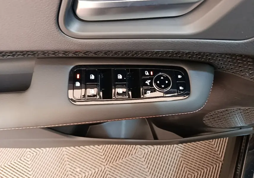 Gros plan sur la commande des vitres et rétroviseurs côté conducteur du Nissan Ariya noir, avec finition cuir et surpiqûres.