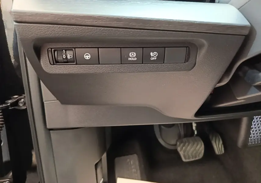 Détail intérieur côté gauche du tableau de bord noir du Nissan Ariya 2026 avec commandes d'assistance et pédales visibles.
