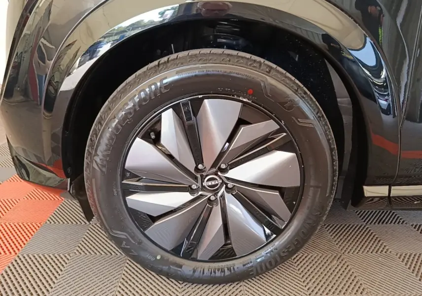 Gros plan sur la roue avant gauche noire du Nissan Ariya 63kWh avec jante argent et noire au design moderne.