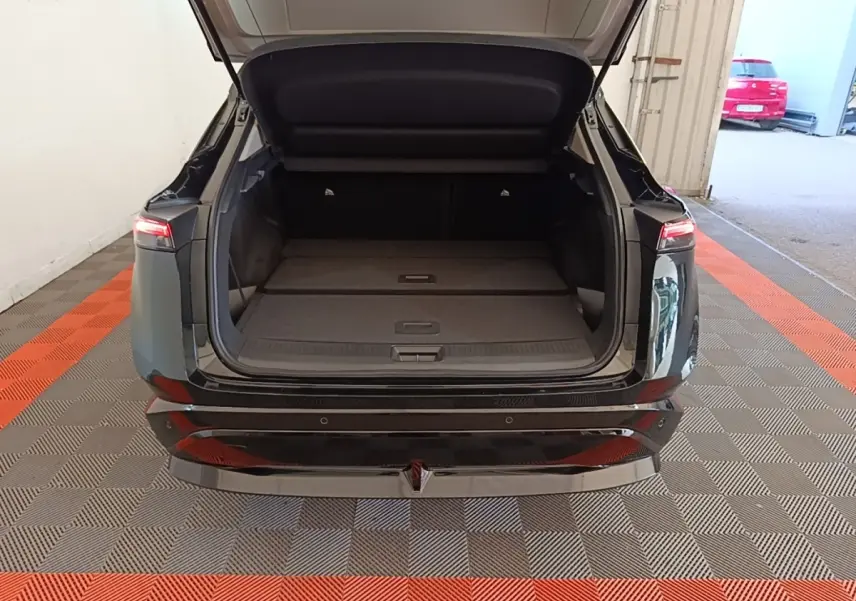 Vue arrière d'un Nissan Ariya noir 2026 avec coffre ouvert et banquette arrière rabattue dans un garage.