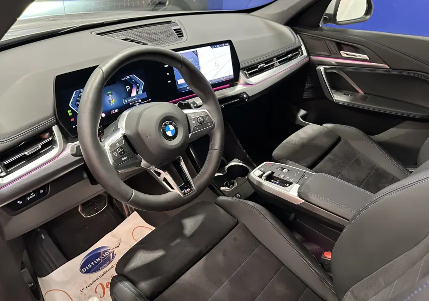 Intérieur avant droit du BMW X1 2024 M Sport avec volant cuir, tableau de bord numérique et sièges sport noirs.