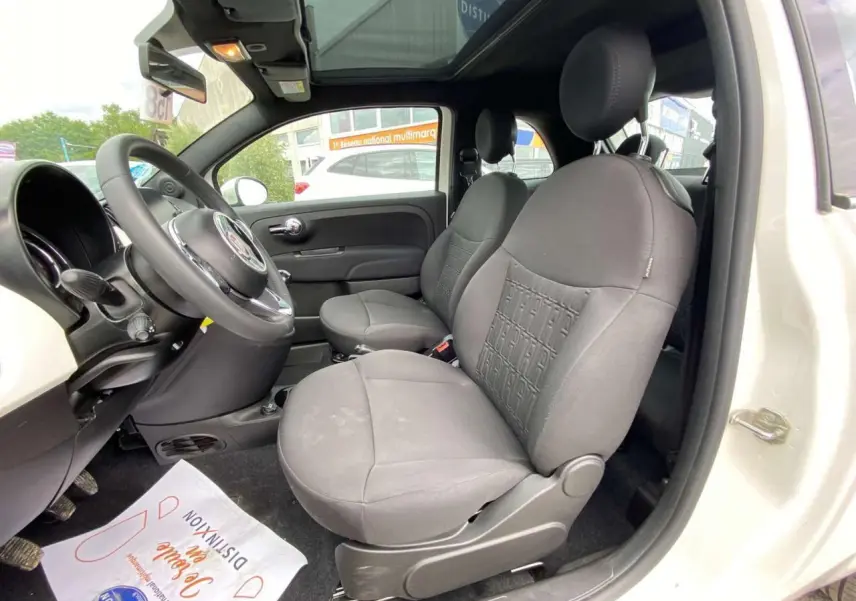 Vue intérieure côté conducteur de la Fiat 500 blanche 2024, mettant en valeur les sièges avant gris et le toit panoramique.