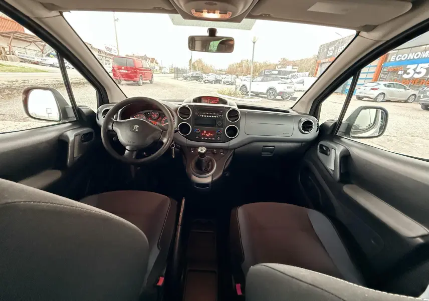 Vue intérieure avant du Peugeot Partner Tepee 2014, montrant le tableau de bord et les sièges en tissu noir et gris.