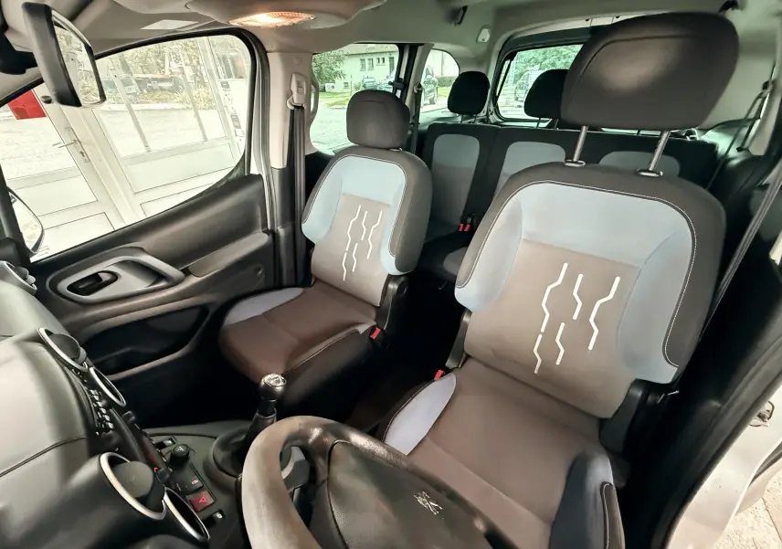 Vue intérieure avant droite du Peugeot Partner Tepee gris, mettant en valeur les sièges tissu noir et bleu avec motifs blancs.