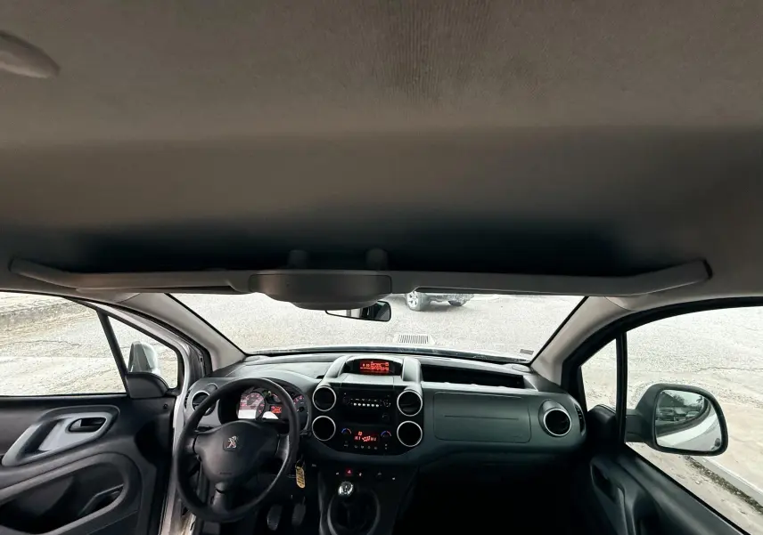 Vue intérieure frontale du Peugeot Partner Tepee gris, montrant le tableau de bord et le volant à gauche.
