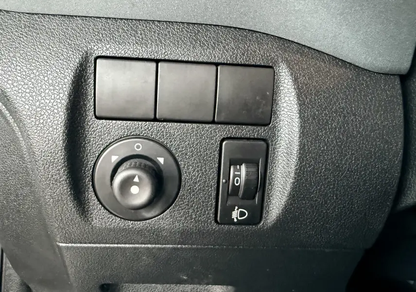 Gros plan sur les commandes de réglage des rétroviseurs et des phares du Peugeot Partner Tepee gris, intérieur noir.