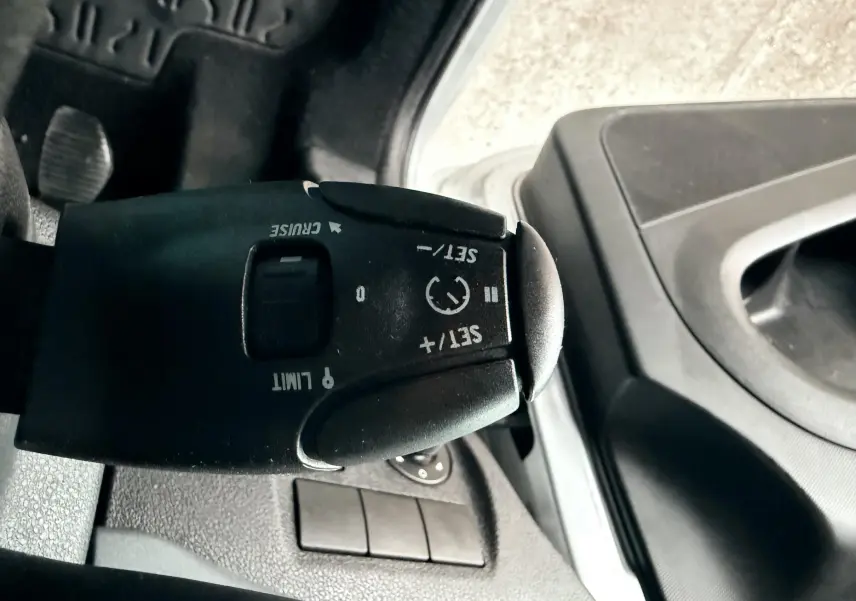 Gros plan sur la commande de régulateur de vitesse noire à gauche du volant dans l’habitacle gris du Peugeot Partner Tepee.