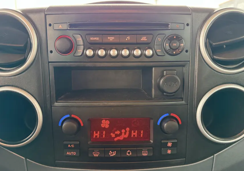 Vue rapprochée du tableau de bord noir et gris du Peugeot Partner Tepee 2014 avec commandes climatisation et autoradio.