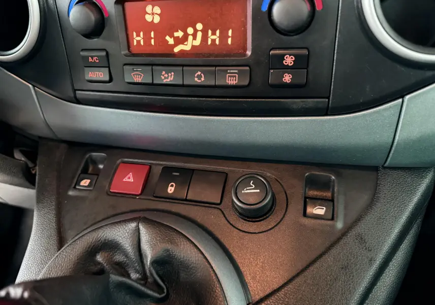 Gros plan sur la console centrale du Peugeot Partner Tepee gris, montrant les commandes de climatisation et le levier de vitesse en cuir noir.