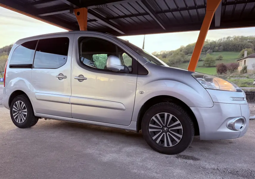 Peugeot Partner Tepee gris vu de profil côté droit, sous abri avec jantes spécifiques et vitres teintées.