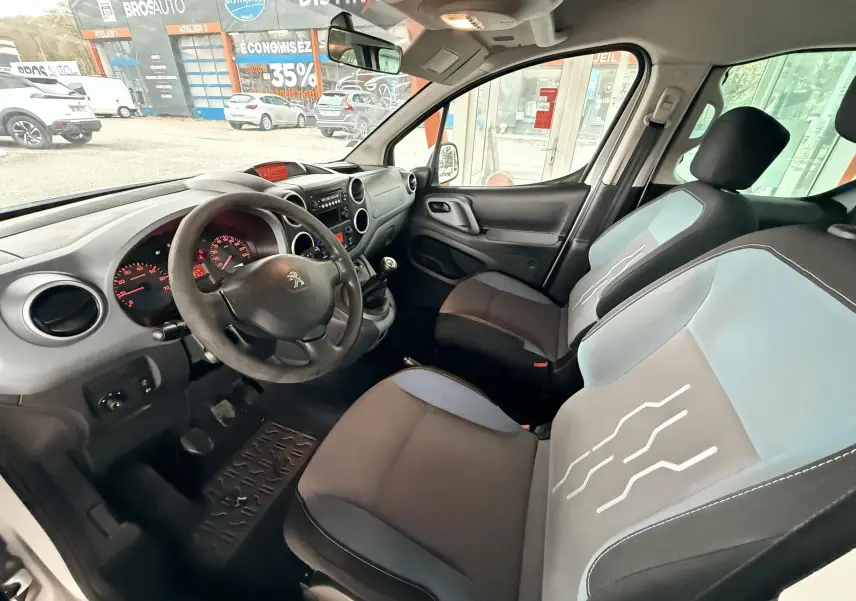 Vue intérieure côté conducteur du Peugeot Partner Tepee gris, mettant en valeur le volant, tableau de bord et sièges tissu bicolores.