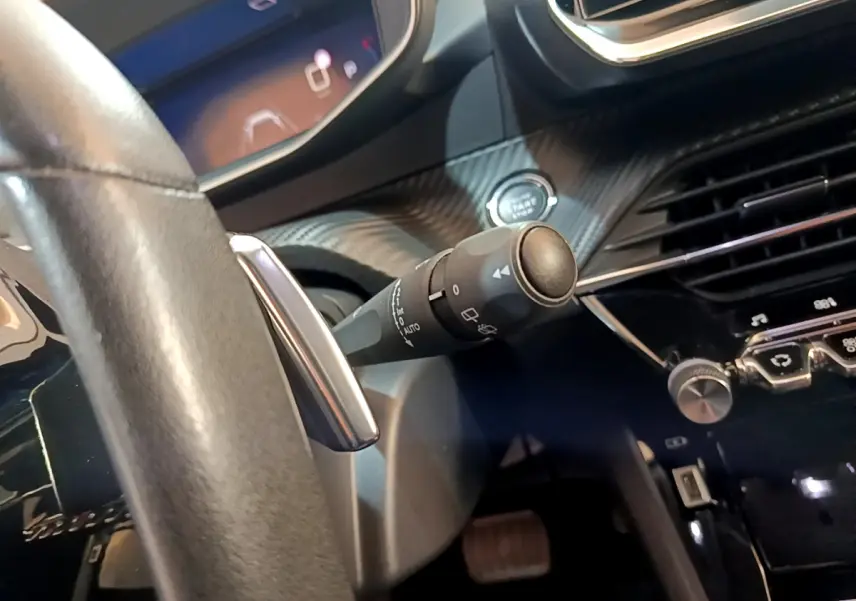 Détail intérieur du Peugeot 2008 2021, vue du volant cuir et commande de phares sur fond de tableau de bord noir.