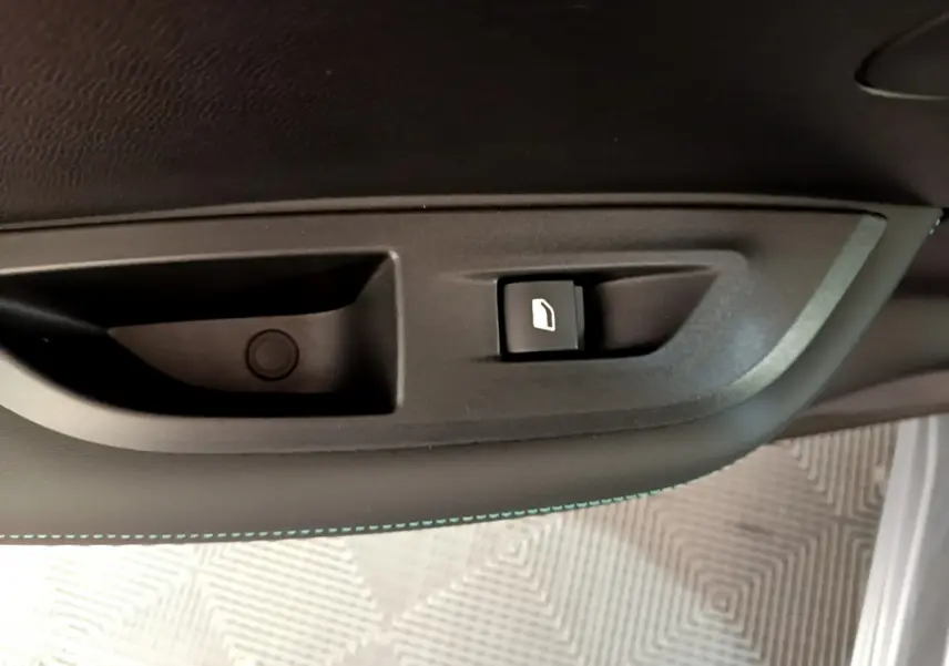 Gros plan sur le bouton d’ouverture de trappe à carburant dans l’habitacle du Peugeot 2008 gris clair, côté conducteur.