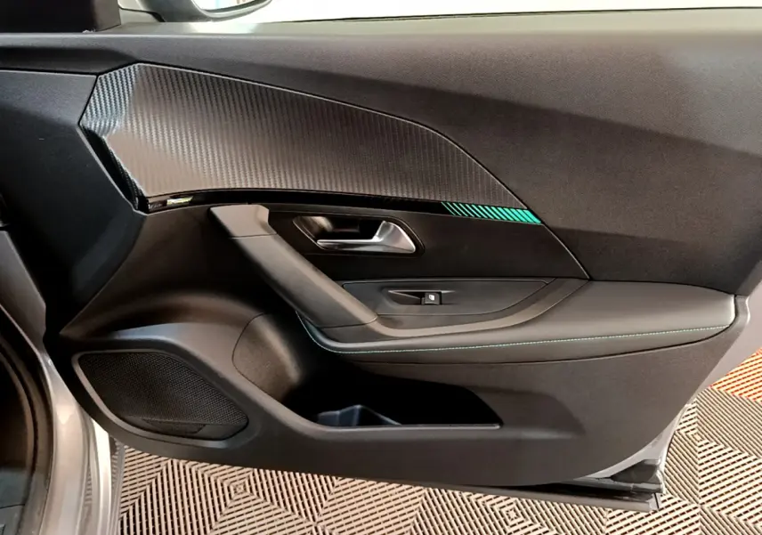 Vue intérieure du panneau de porte avant gauche du Peugeot 2008 gris clair, avec insert imitation carbone et surpiqûres bleues.