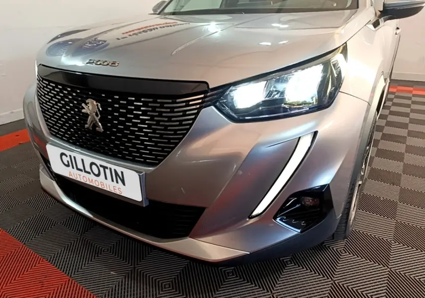 Vue 3/4 avant droit d'un Peugeot 2008 gris clair avec phares LED allumés et calandre noire distinctive.