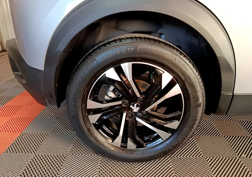 Gros plan sur la roue avant droite du Peugeot 2008 gris clair, mettant en valeur la jante noire et argentée.