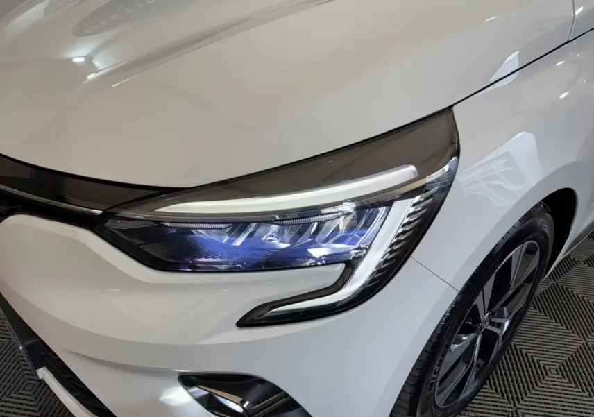 Gros plan sur le phare avant droit LED et la roue alliage noire d'une Renault Clio Business blanche 2023.