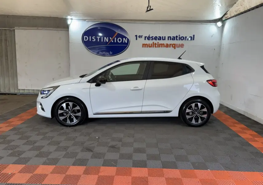 Profil droit d'une Renault Clio blanche 2023 Business TCe 100 GPL, avec jantes alliage et rétroviseurs noirs dans un garage.