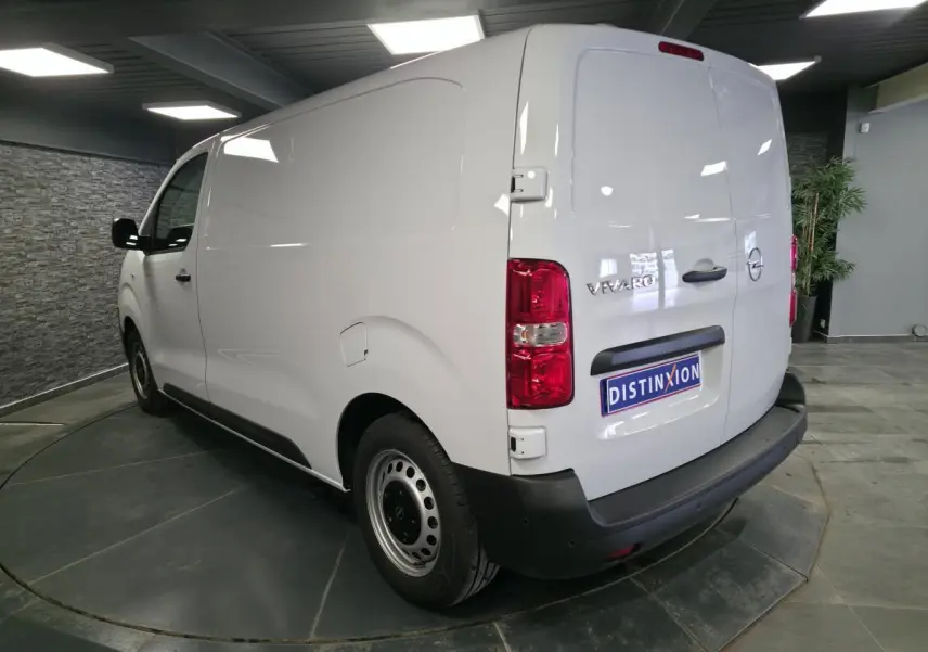 Vue 3/4 arrière droite d’un Opel Vivaro blanc avec portes arrière battantes et jantes tôles grises en intérieur showroom.