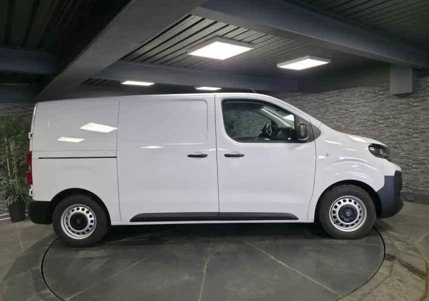 Opel Vivaro blanc en vue de profil côté gauche dans un showroom avec jantes tôles et poignées noires.