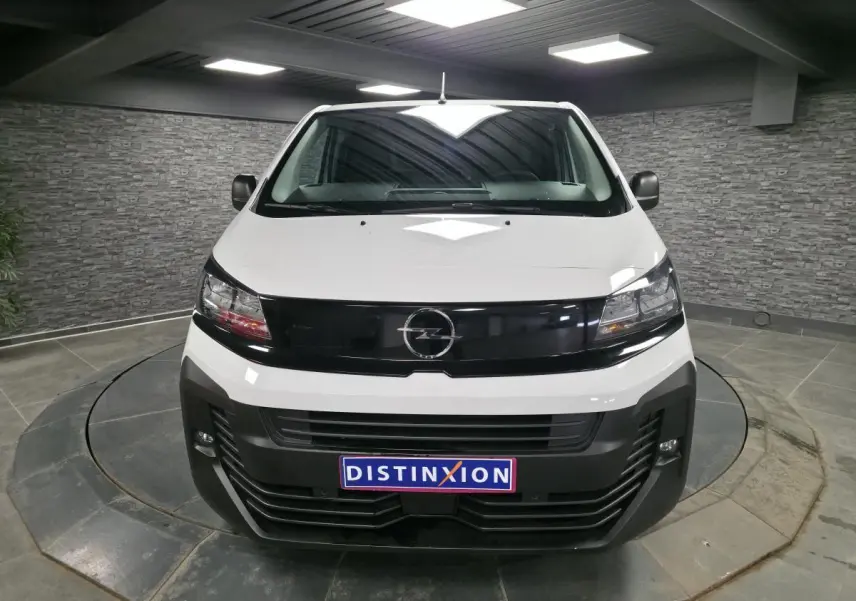 Vue avant d'un Opel Vivaro blanc 2025 avec calandre noire brillante et projecteurs modernes, en intérieur showroom.