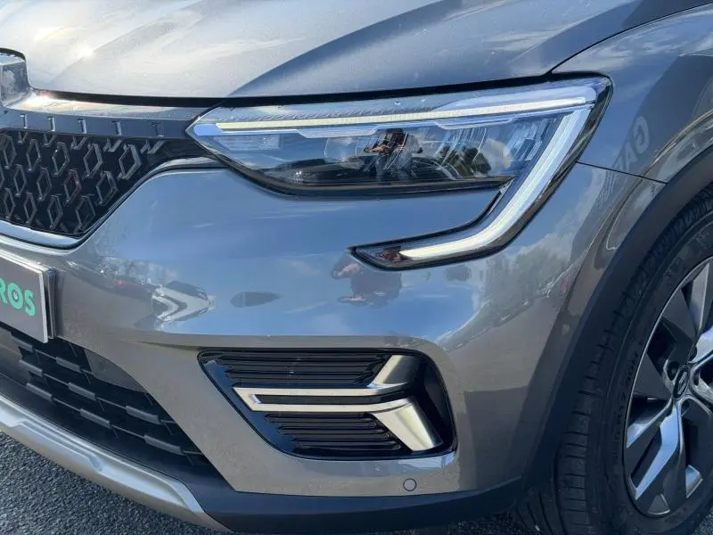 Gros plan sur l’avant droit du Renault Arkana gris métallisé 2025, mettant en valeur le phare LED et la calandre distinctive.